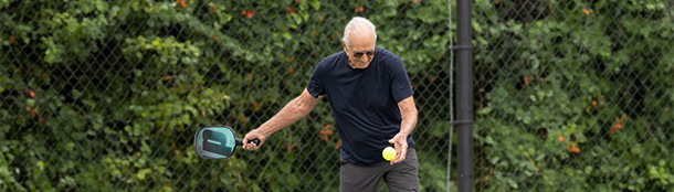 Older man swinging a pickle ball racket